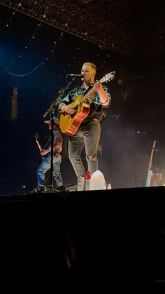 a man standing on top of a stage with a guitar in his hand and other people behind him