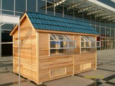 a small wooden building with a blue roof and windows on the outside, in front of a large glass window