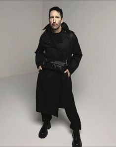 a man in a trench coat posing for the camera with his hands on his hips