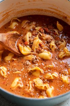 a pot filled with pasta and sauce on top of a wooden spoon in the bowl