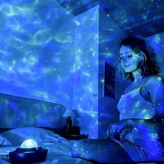 a woman is sitting on her bed in the room with blue lights and stars all around