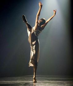 a woman is dancing on stage with her arms in the air and one leg up