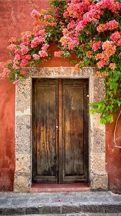 an open door with pink flowers growing over it's sides and on the outside