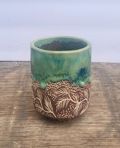 a green and brown pot sitting on top of a wooden table next to a white wall