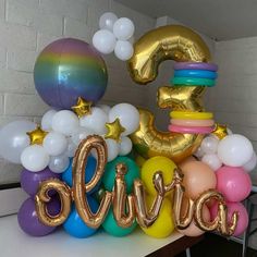 a table topped with balloons and heliums that spell out the number three in different colors