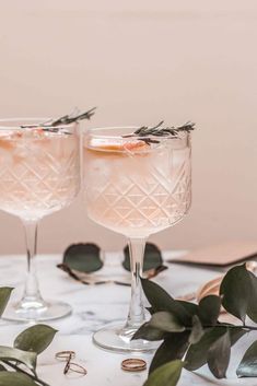 two glasses filled with pink wine and garnished with greenery on a marble table