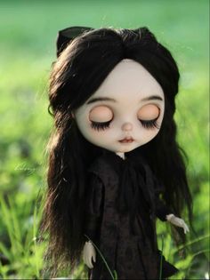 a doll with long black hair is standing in the grass and has her eyes closed