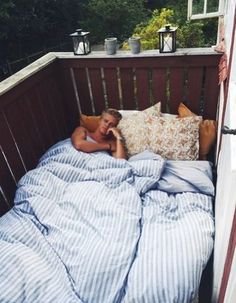 a woman laying in bed on top of a wooden porch