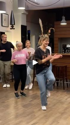 a group of people are dancing in a room with wood flooring and lights hanging from the ceiling