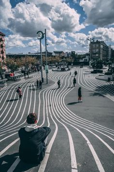 a person sitting on the ground looking at something in the distance with buildings and clouds behind them