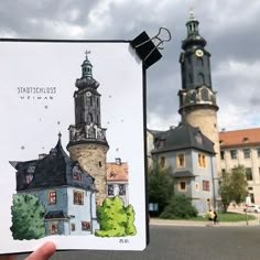 a hand holding up a card with an image of a building and two towers in the background