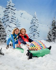 two women sitting on an inflatable snow sleigh with trees behind them