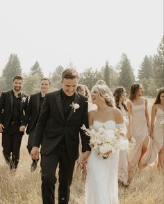 a bride and groom walking through tall grass with their bridal party in the background