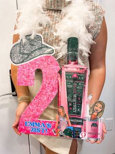 a woman holding up a pink number two sign and perfume bottle in front of her face