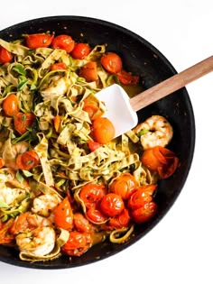 a skillet filled with pasta and shrimp next to a wooden spoon on a white surface