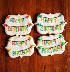 four decorated cookies sitting on top of a wooden table with happy birthday written on them