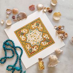 an art work with shells and beads on the table next to it is a blue beaded necklace