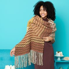 a woman standing in front of a blue wall wearing a brown and white knitted shawl