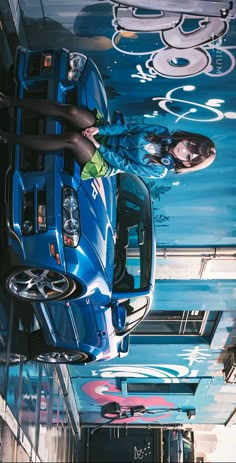 a woman standing next to a blue sports car in a garage with graffiti on the ceiling