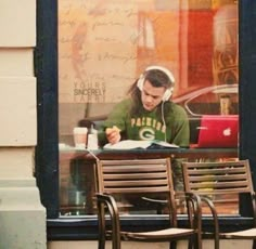 a man sitting at a table in front of a store window with headphones on