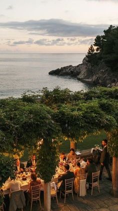 an outdoor dining area overlooking the ocean with people sitting at tables in front of it