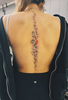 the back of a woman's neck with flowers and leaves tattooed on her lower back