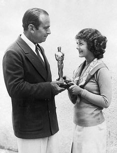 an old black and white photo of a man holding a trophy next to a woman