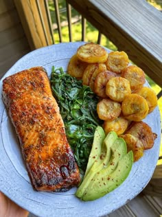 a plate with salmon, spinach, potatoes and avocado on the side