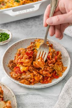 a person holding a fork in a bowl filled with pasta and meat casserole