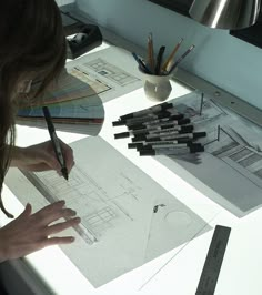 a woman sitting at a table working on architectural drawings and pencils in front of her