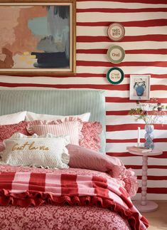 a red and white striped wall in a bedroom next to a bed with pillows on it