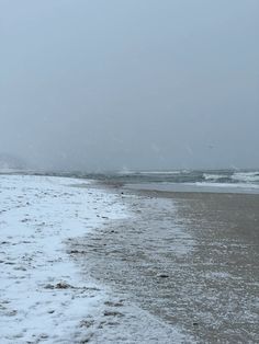 the beach is covered in snow and has footprints leading to the water's edge