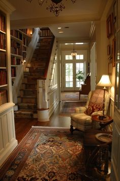 a living room filled with lots of furniture and bookshelves next to a stair case