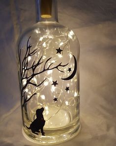 a glass bottle with a dog and tree on it is lit up by fairy lights