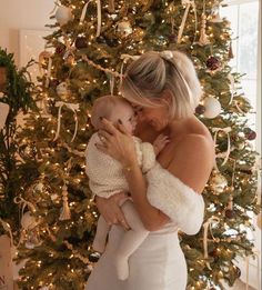 a woman holding a baby in front of a christmas tree