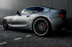 a silver sports car parked in front of a building with red rims on it