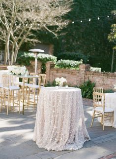 a table with white flowers on it in the middle of a courtyard area, surrounded by chairs and tables