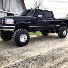 a black pickup truck parked in front of a barn with large tires on it's flatbed