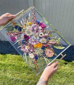 a person holding up a glass box with flowers in it on top of the grass