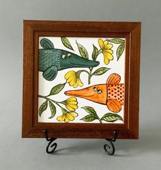 a small wooden frame with an orange fish and green alligators on it's sides