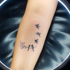 a small tattoo on the arm of a woman with birds flying around her wrist and tree branch