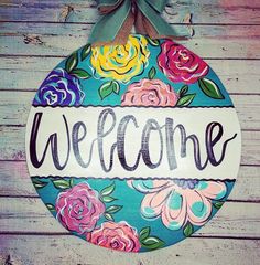 a welcome sign hanging on the side of a wooden wall with flowers painted on it