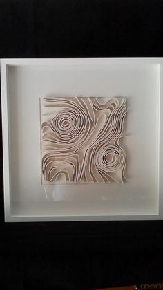 an abstract paper sculpture in a white frame on a black background with a wooden table next to it