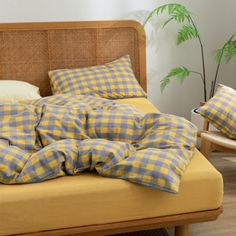 a bed with yellow and blue checkered sheets in a room next to a plant