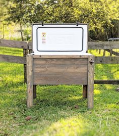 an old cooler sitting on top of a wooden bench in the grass next to a fence