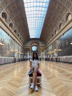 a woman is sitting on a bench in the middle of a room with many paintings