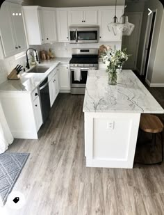 a kitchen with white cabinets and marble counter tops