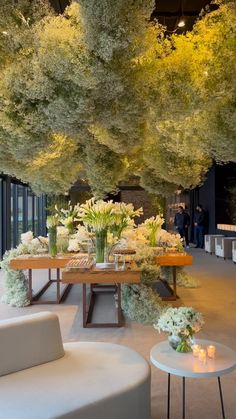 a room filled with lots of white flowers and greenery next to tables covered in trees