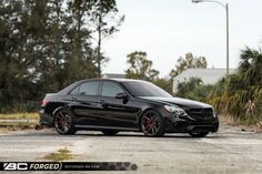 a black car parked on the street in front of some palm trees and bushes with red rims