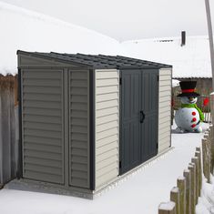 a small storage shed in the snow with a snowman next to it